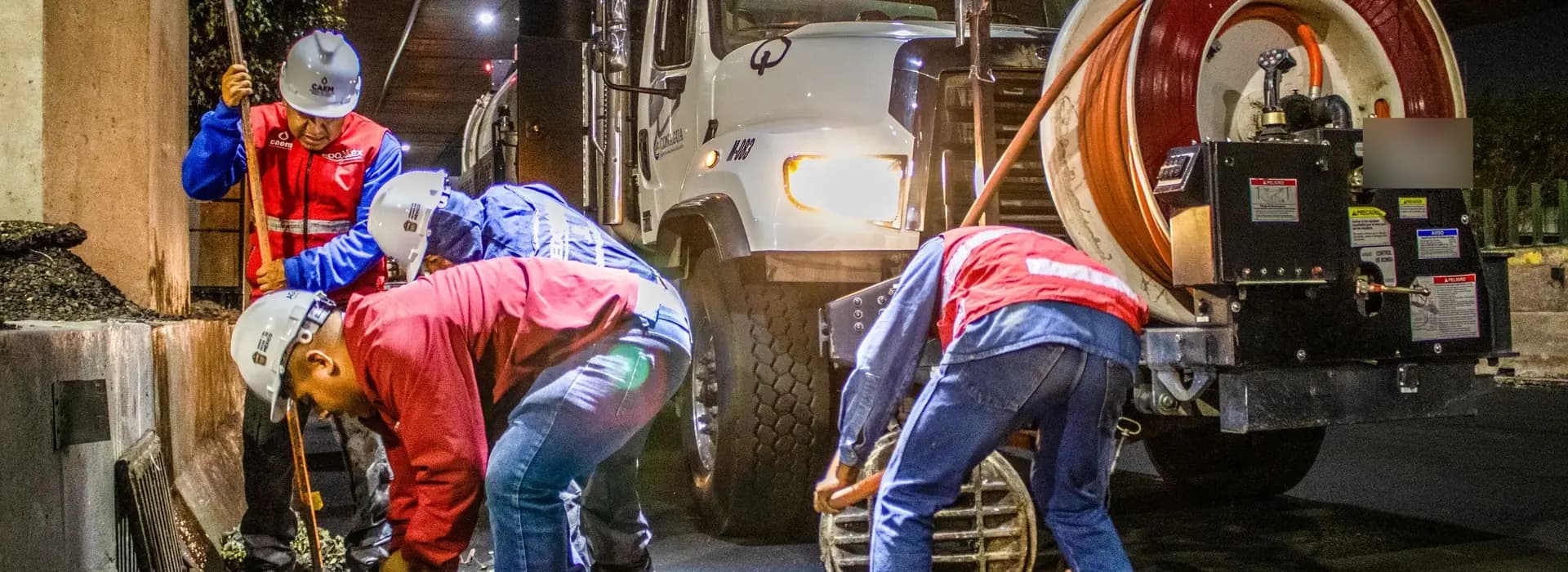 Drainage crew in hard hats and safety gear working beside a jetting tanker