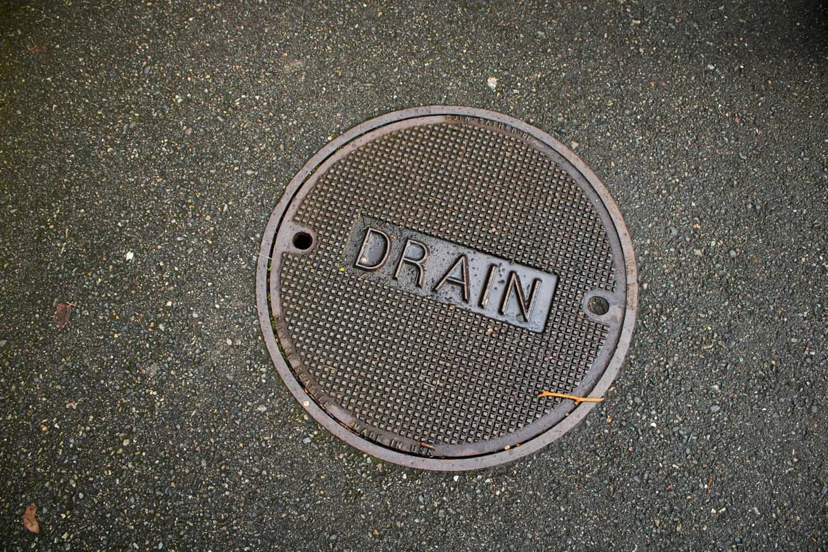 Round metal manhole cover stamped with the word DRAIN set into a tarmac surface